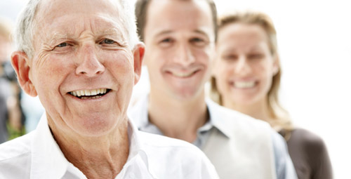 An older smiling gentleman stood with a younger man and woman also smiling