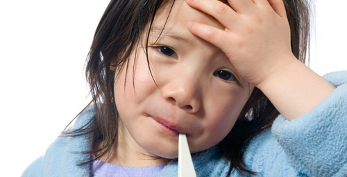 A young girl who looks ill holding her hand to her forehead with a thermometer in her mouth